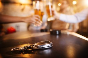 car-keys-laid-on-a-bartop-with-two-people-holding-glasses-of-beer-in-background