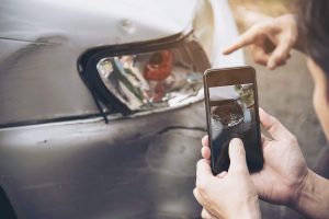 hit and run accident victim and witness take pictures of broken headlights, fender, and bumper of a silver car