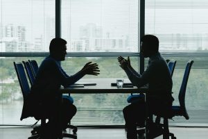 Personal Injury Attorney and Insurance Company Attorney Negotiating a Settlement at Table Overlooking Office Park