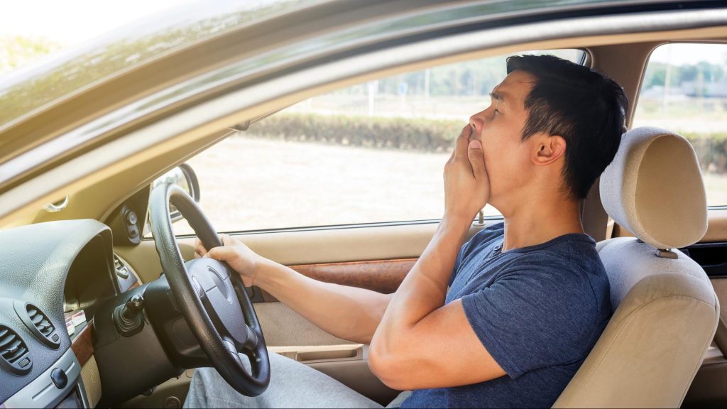 A drowsy driver yawns as he is about to fall asleep behind the wheel