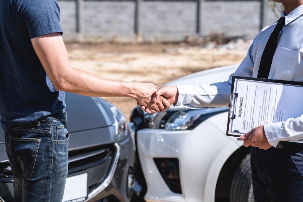 a driver and an insurance agent shake hands at the scene of an accident