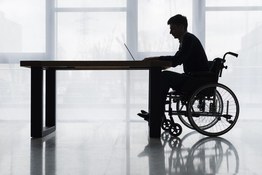 silhouette of a man in a wheelchair at a table using a laptop computer