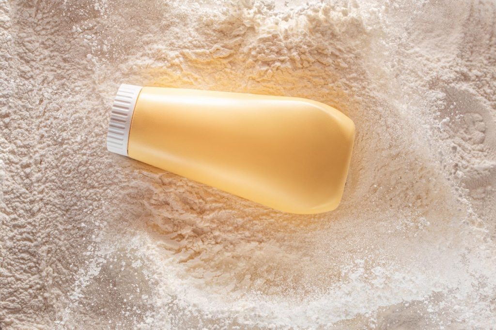 A yellow plastic bottle sitting on top of a thick layer of talcum powder. Regular usage of talc powder for genital hygiene has been linked to ovarian cancer and mesothelioma.