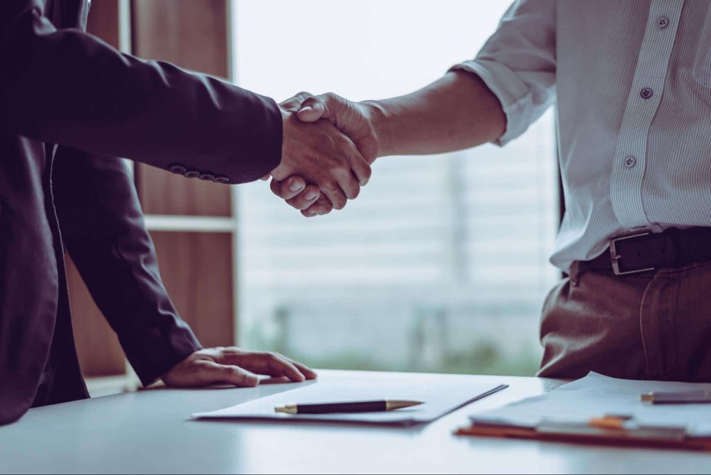 An injured worker and an attorney shake hands after calculating a workers' compensation settlement.