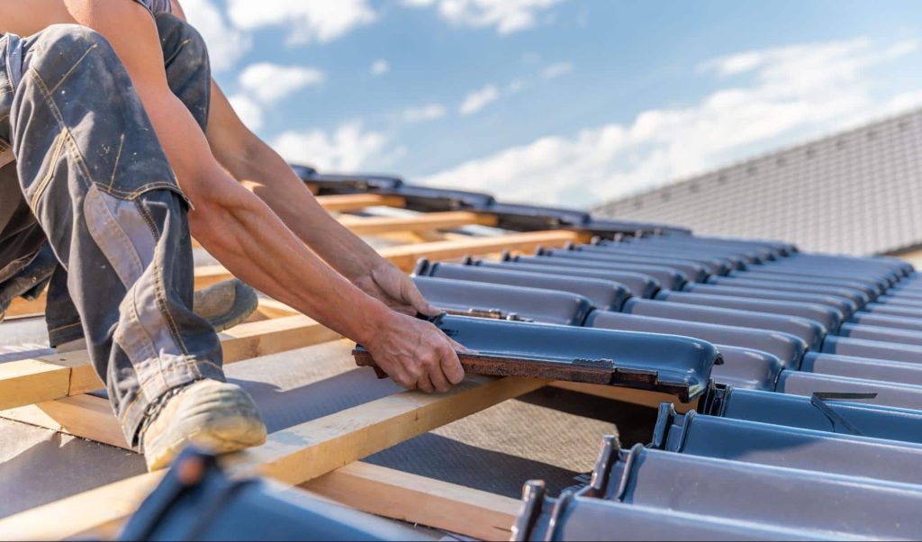 A roofer places tiles on a new roof. If the roofer gets injured at work, they may require a workers' compensation settlement.