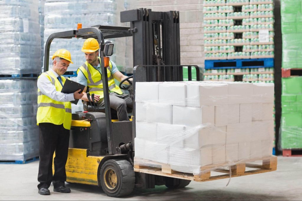 A forklift operator stops to speak with his supervisor. If the forklift operator is injured at work he would need to report the injury to human resources or a safety officer to file a workers comp claim.