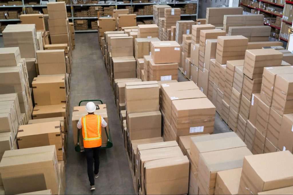 A worker pushes a cart with boxes through a warehouse.