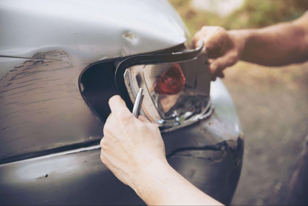 An insurance adjuster inspects a broken car headlight after a minor car accident.