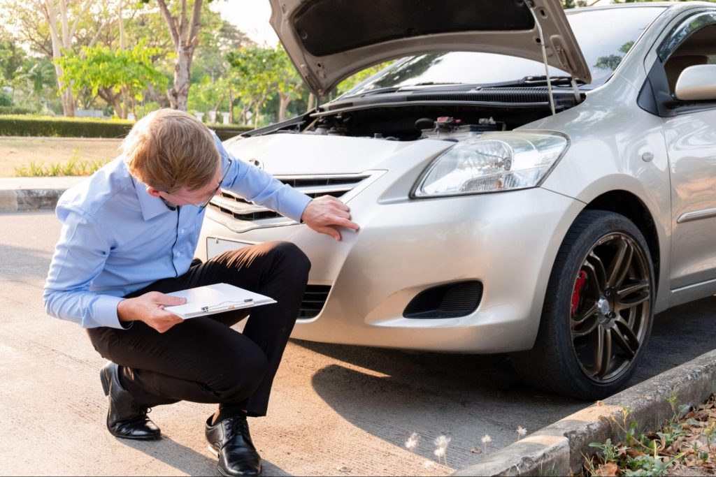 An insurance adjuster inspects a damaged car after a small accident.