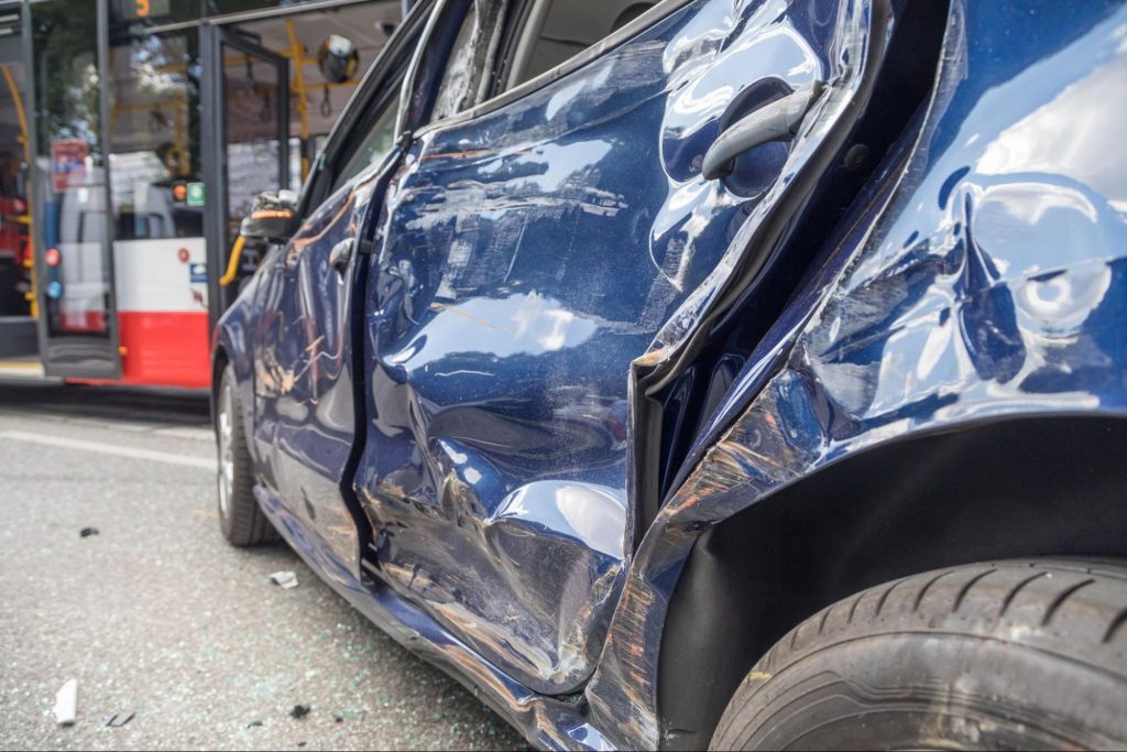 A blue car which has been totaled due to a side impact collision with an uninsured driver.