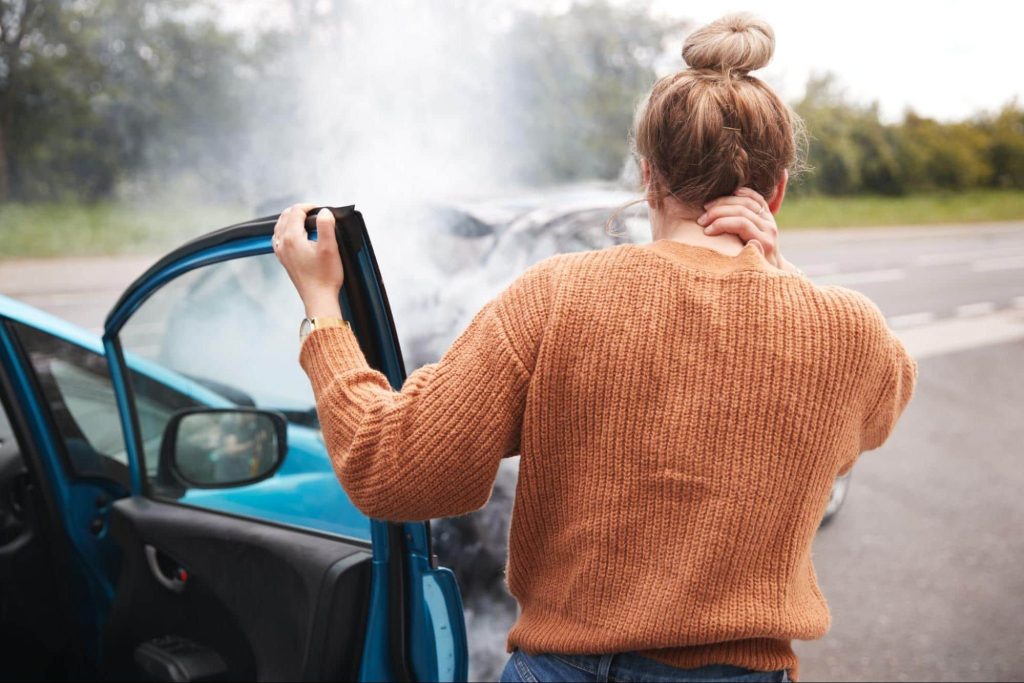 A woman holding her hand to her-injured neck while getting out of a car after a rear end accident.