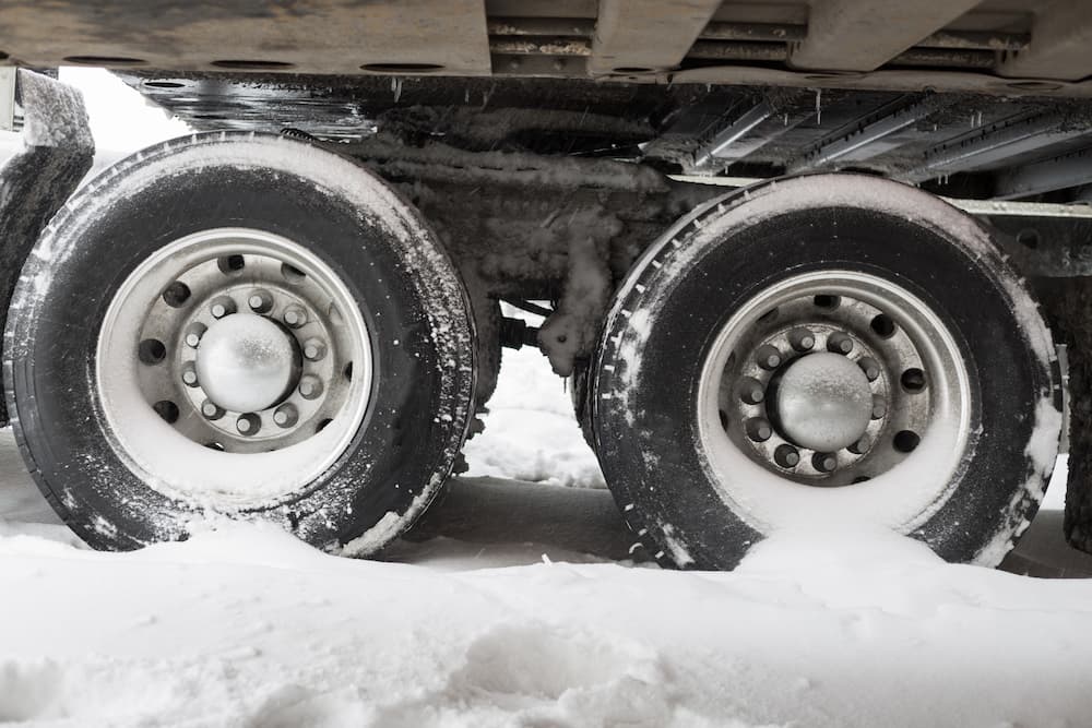 Close-up of 18-wheeler truck tires stuck in deep snow, illustrating dangerous road conditions for 18-wheeler accidents in Kentucky.